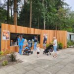 Mit Holzplanken abgedeckter Container neben einem Wald.