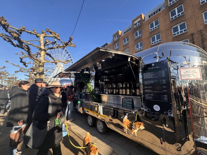 Vintage-inspirerad strömlinjeformad matvagn som serverar glögg till besökare på en livlig julmarknad upplyst av festliga ljus.